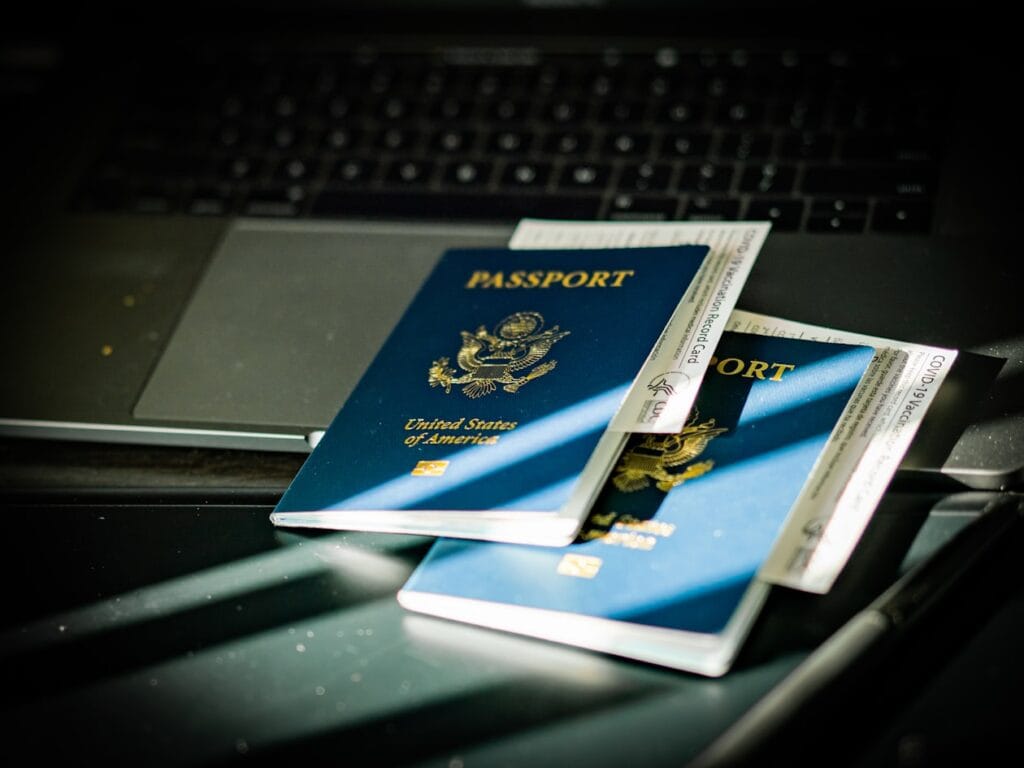 Two United States passports and travel documents on a keyboard-lit desk, suggesting travel prep at a computer.