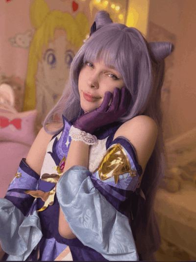 Cosplayer with lavender wig and cat-ear headband, in a purple-blue fantasy costume, resting her chin on a gloved hand in a pastel pink room.