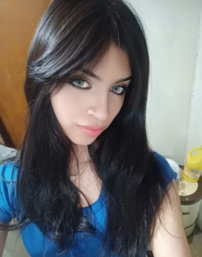 Close-up of a woman with long dark hair and blue eyes, wearing a blue top and looking at the camera.